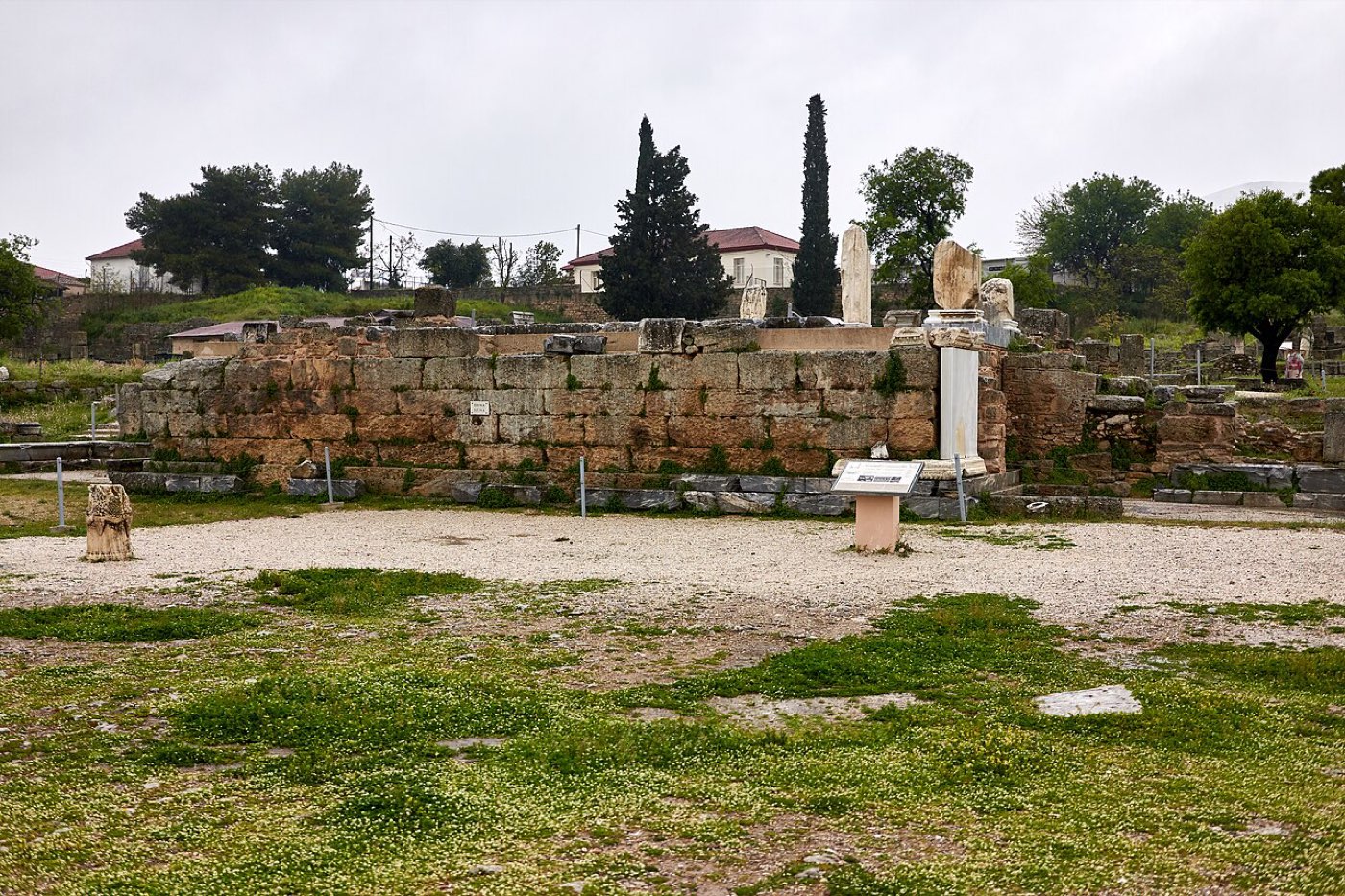 The stone platform of the bema in the forum of ancient Corinth, with broken columns and the excavated marketplace around it.