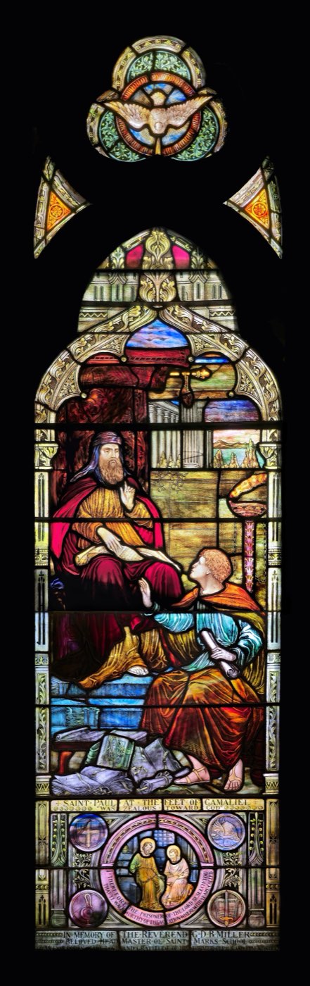 A stained-glass window of the young Saul sitting at the feet of the enthroned rabbi Gamaliel, scrolls scattered around them, inscribed 'Saint Paul at the feet of Gamaliel.'