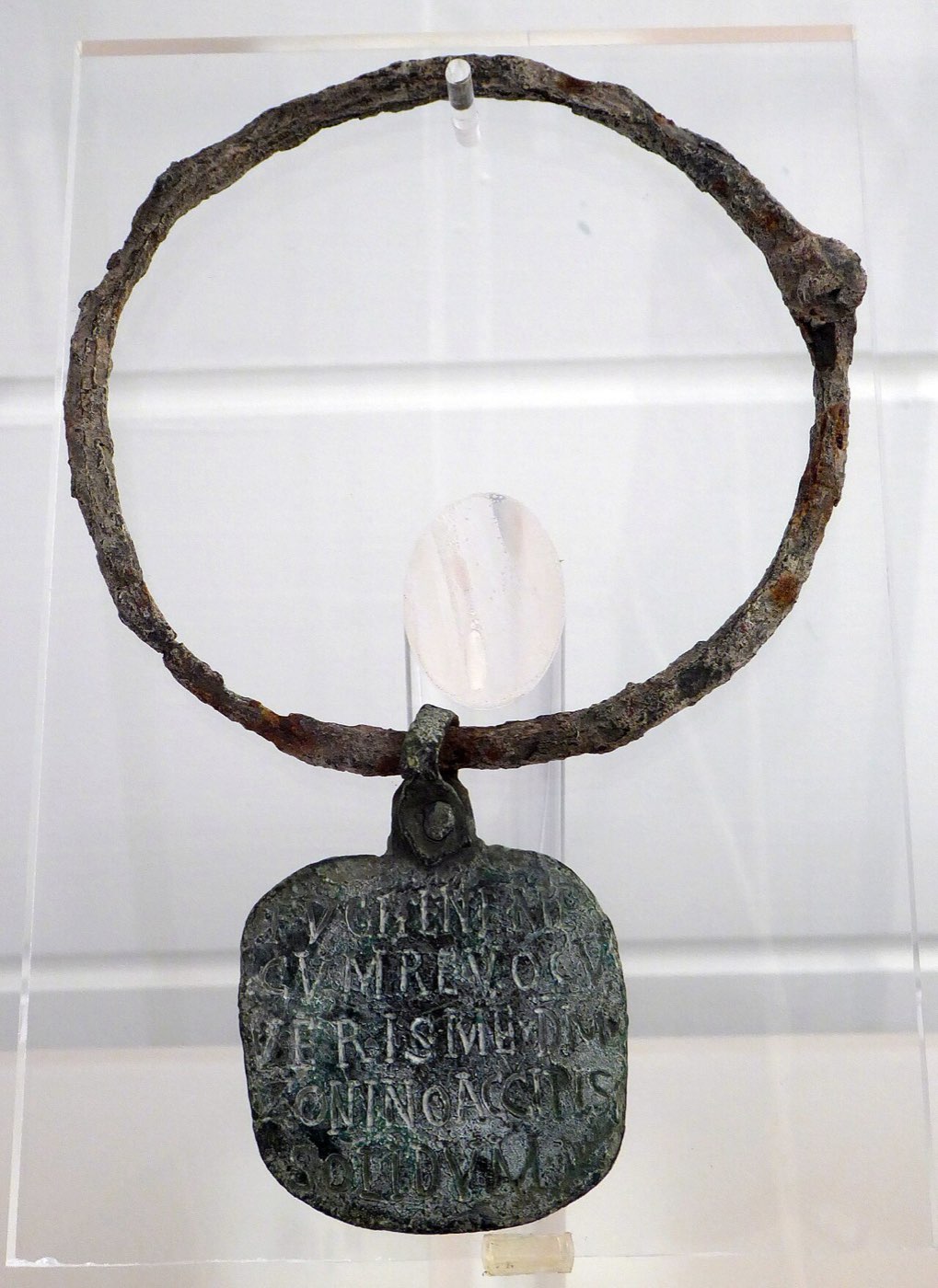 An inscribed bronze Roman slave collar with its iron ring, promising a reward for the return of the runaway who wore it.