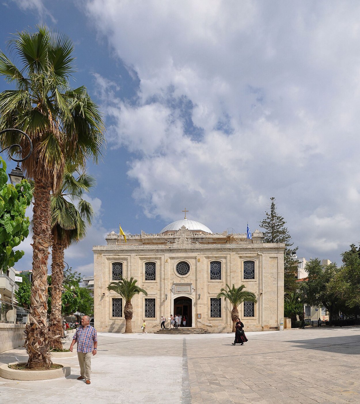 The church of Agios Titos in Heraklion, Crete: a domed stone basilica on a sunlit square with palm trees.