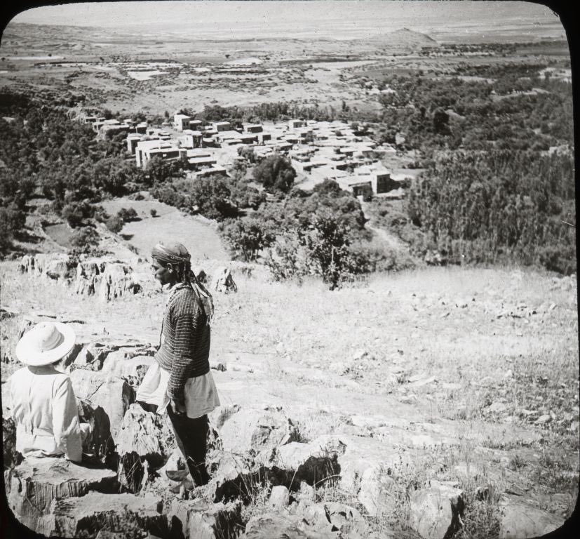 An early photograph of Banias, ancient Caesarea Philippi: village houses among trees below a rocky cliff, with figures resting in the foreground.