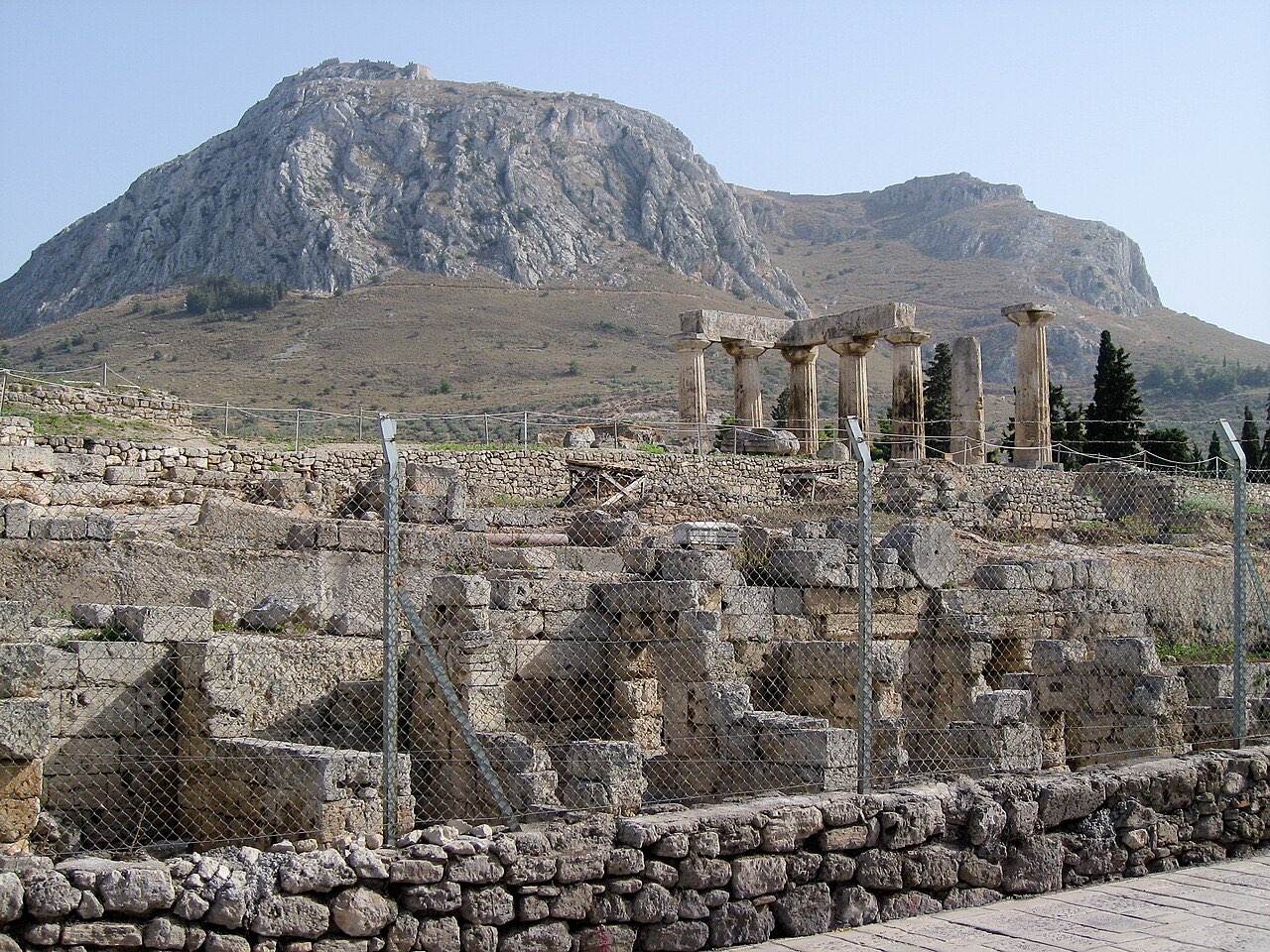 The Doric columns of the Temple of Apollo at ancient Corinth, with the fortress-topped mountain of Acrocorinth rising behind.