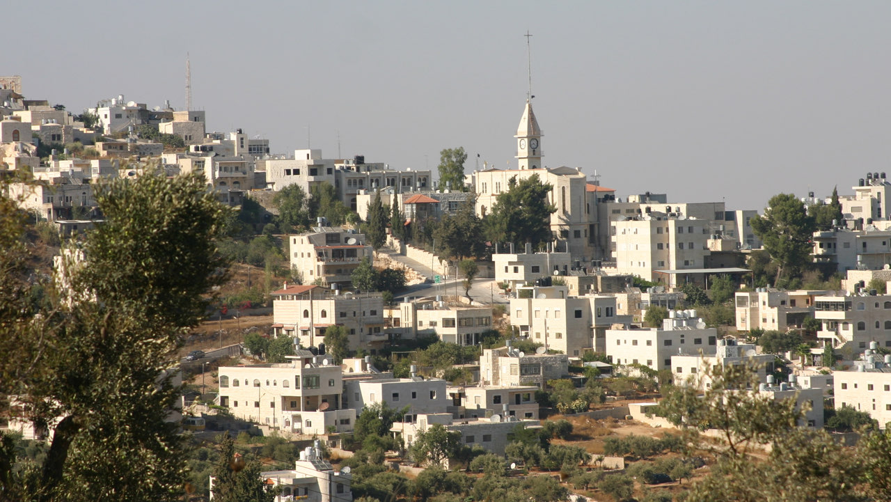 The hilltop village of Taybeh: stone houses and a church tower clustered on a ridge under a pale sky.