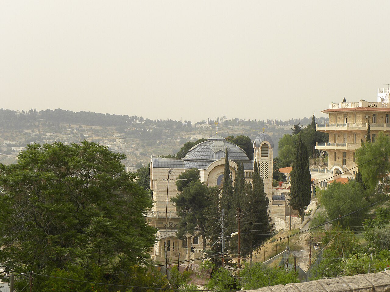 The Church of St. Peter in Gallicantu on the slope of Mount Zion: a modern stone church with a golden rooster atop its cross, terraces and trees around it.