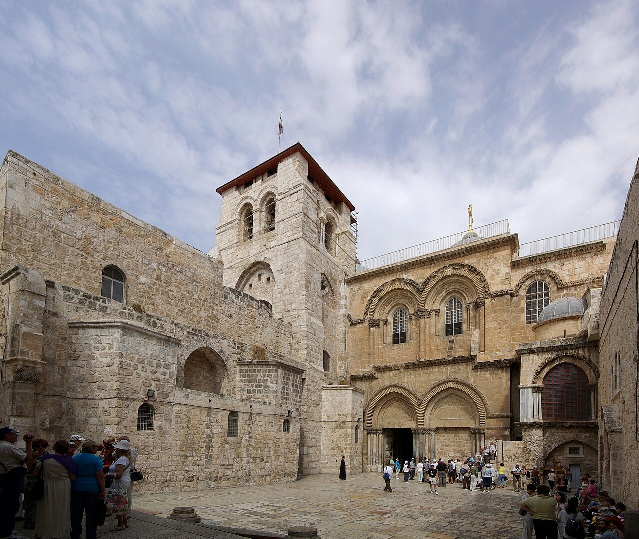 The weathered stone facade and twin arched doorways of the Church of the Holy Sepulchre, with its courtyard in front.