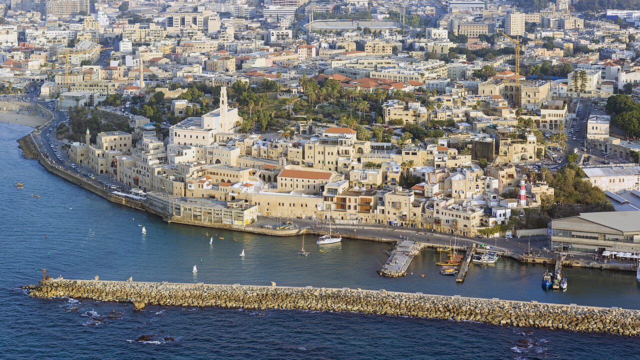 Aerial view of Old Jaffa: the stone old city on its headland, the small crescent harbor with boats, and the sea beyond.