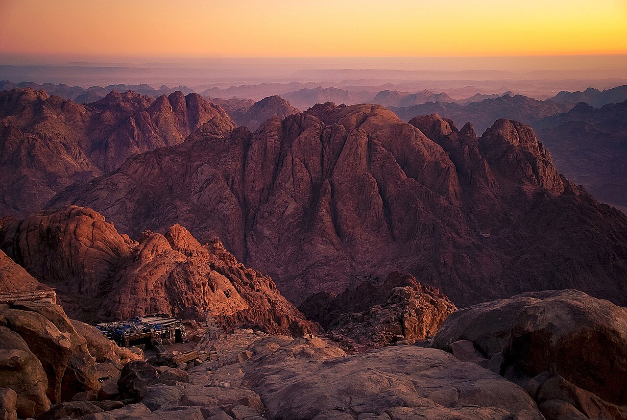 Sunrise over the granite peaks of the Sinai range from the summit of Jebel Musa, ridges fading into golden haze.