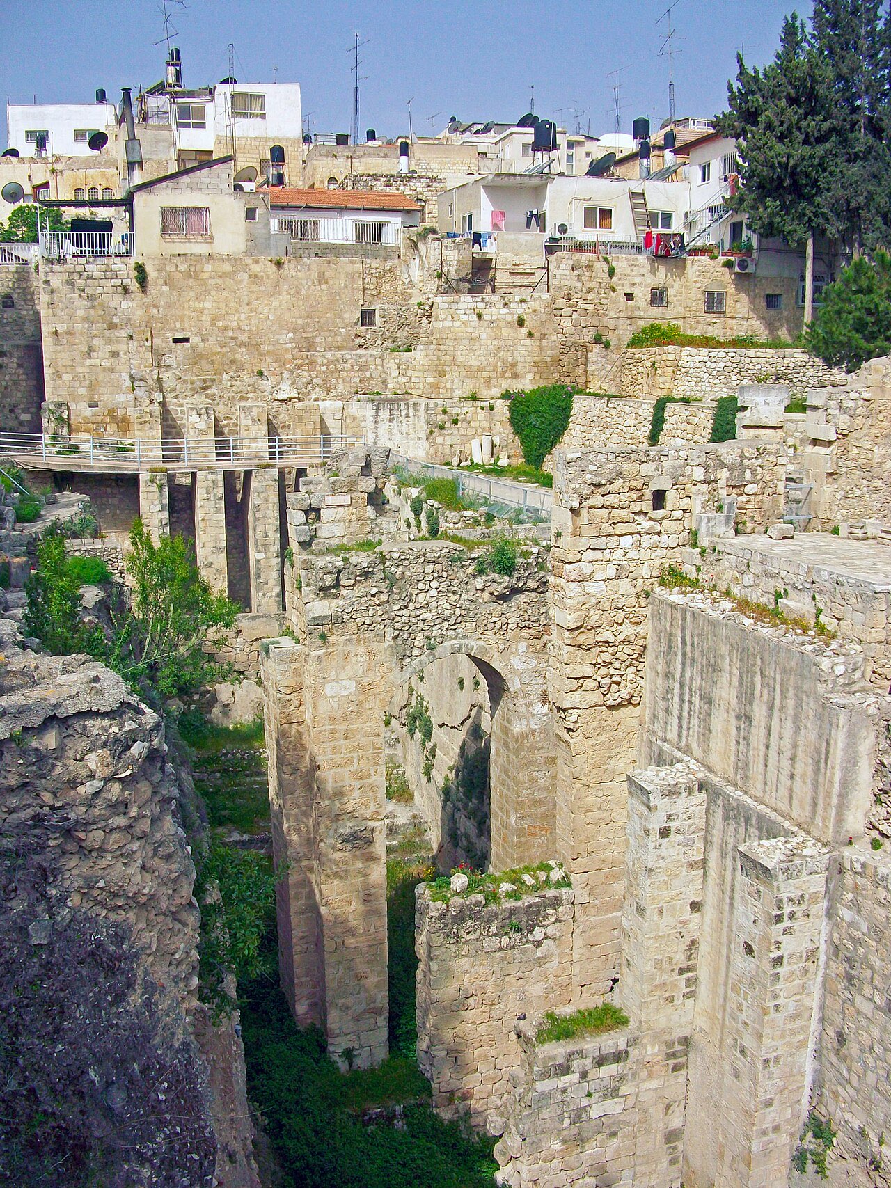 Deep excavated ruins of the Pool of Bethesda: massive stone walls, arches, and column fragments descending well below the modern street level.